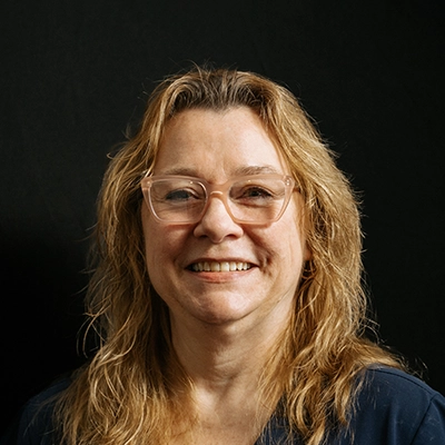 Office Manager Theresa Krajewski Smiling In Front Of Dark Background