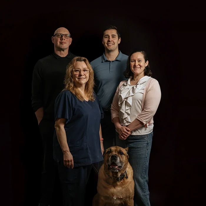 Chiropractor Luke Dijkstra And Adam Mitola With Team Smiling In Front Of Dark Background